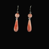 A pair of dangle earrings with round peach-pink coral beads and teardrops, displayed on a black velvet jewelry stand.