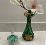 Green perfume bottle with a green and  gold vase with white flowers on a marble surface